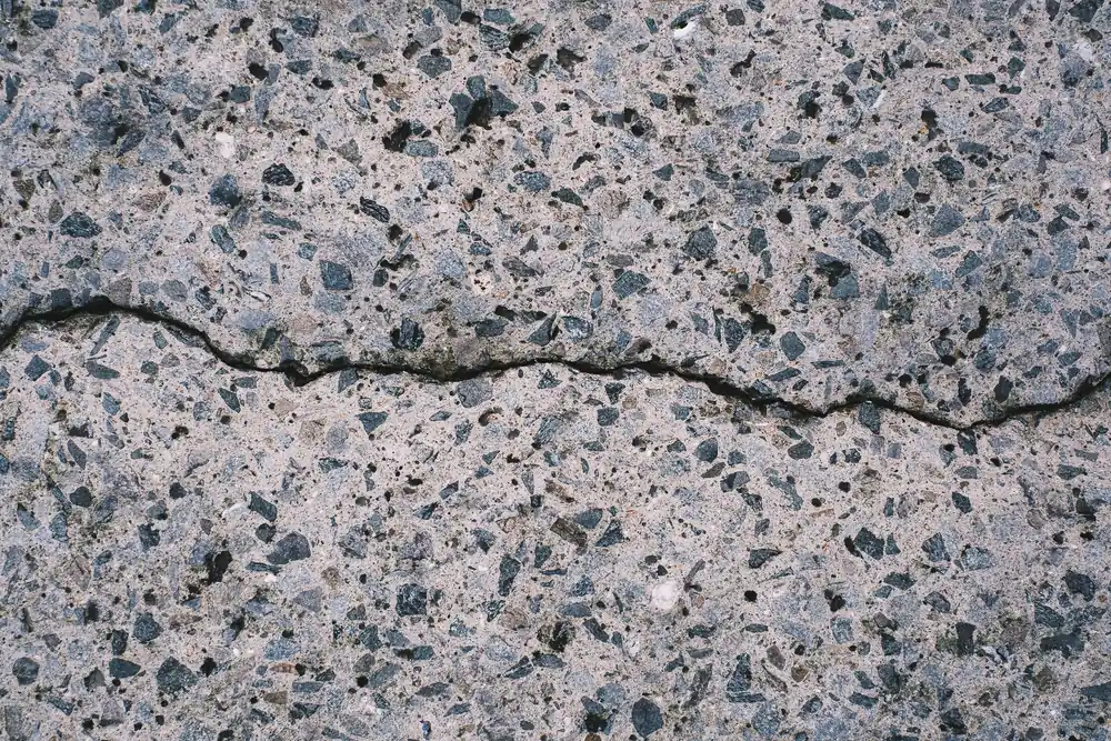 Weathered concrete surface with worn paste, exposed stone and a jagged crack across it