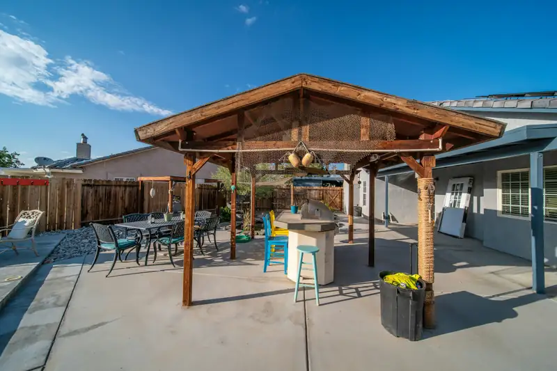 Large broom-finished concrete backyard patio with a wooden gazebo and patio furniture