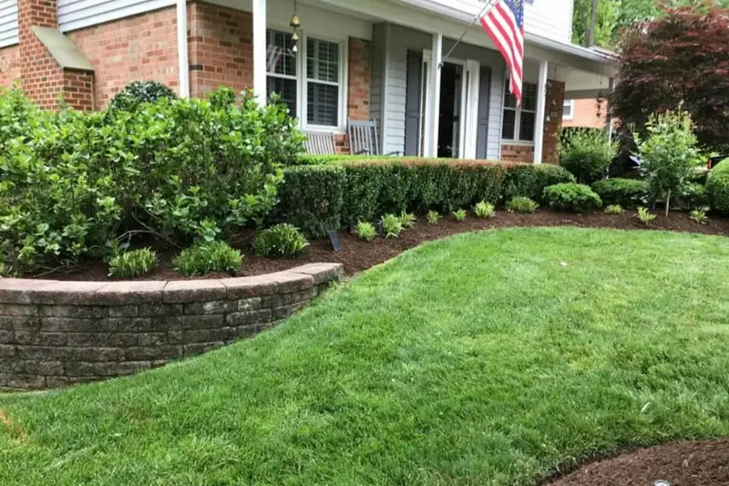 Low curved segmental block retaining wall holding a mulched shrub bed above a front lawn