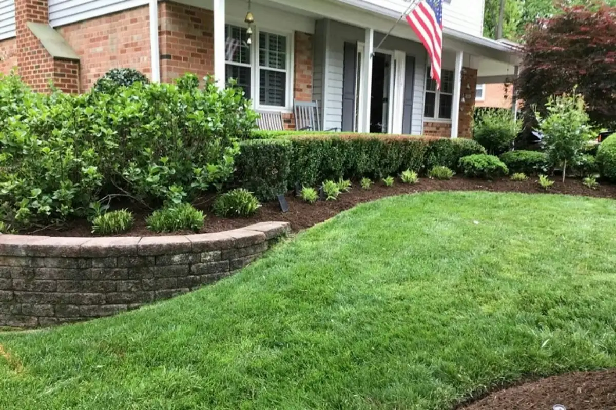 Low curved segmental block retaining wall holding a mulched shrub bed above a front lawn