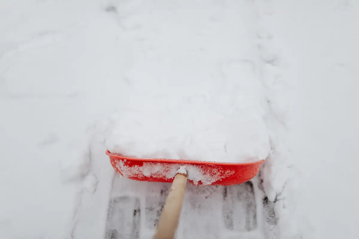 Red snow shovel clearing fresh snow from paving