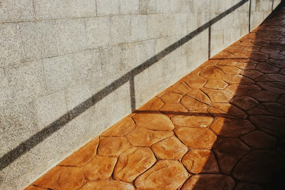 Terracotta-colored stamped flagstone concrete walkway beside a textured gray wall